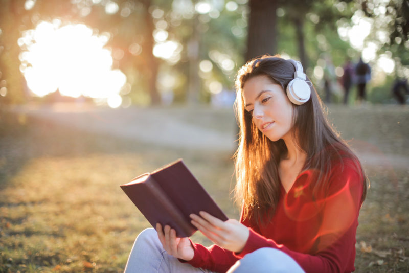 woman-reading-book-while-listening-to-music-on-headphones