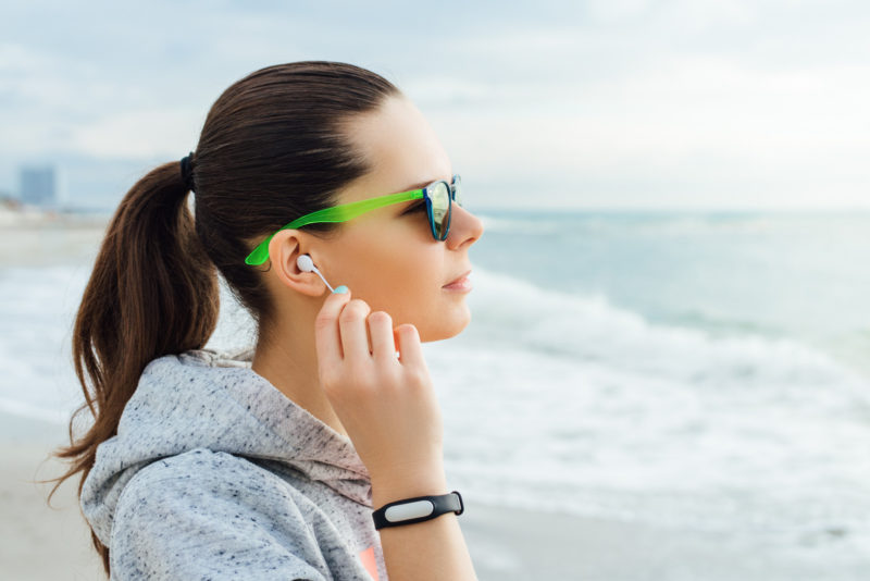 Portrait of brunette listening to music on headphones in the early morning on the beach