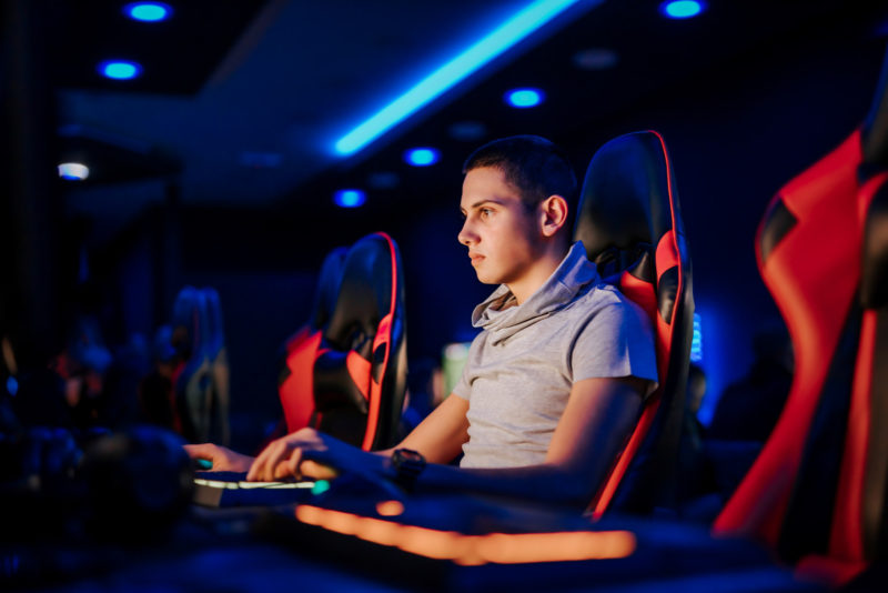 Portrait of a young man playing video game, sitting in a gaming chair, at internet cafe or playroom.