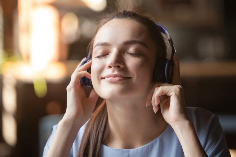 Smiling beautiful millennial girl wearing modern Bluetooth earphones enjoy music playing, happy young woman in headphones listen to favorite tracks like quality sound beats. New technology concept