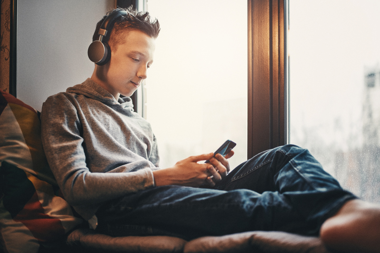Teenager Listening to Music in Headphones Sitting Near Window