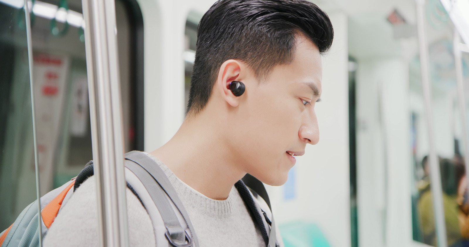 asian man use wireless earbuds to listen music on the mrt train