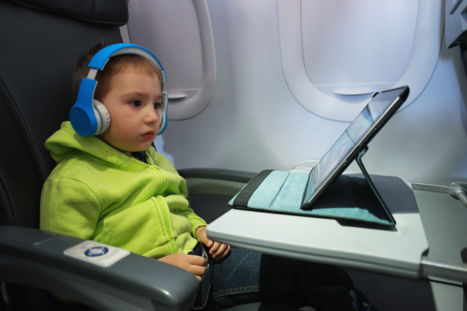 Youn boy sitting in airplane sit watching digital tablet and wearing headphones
