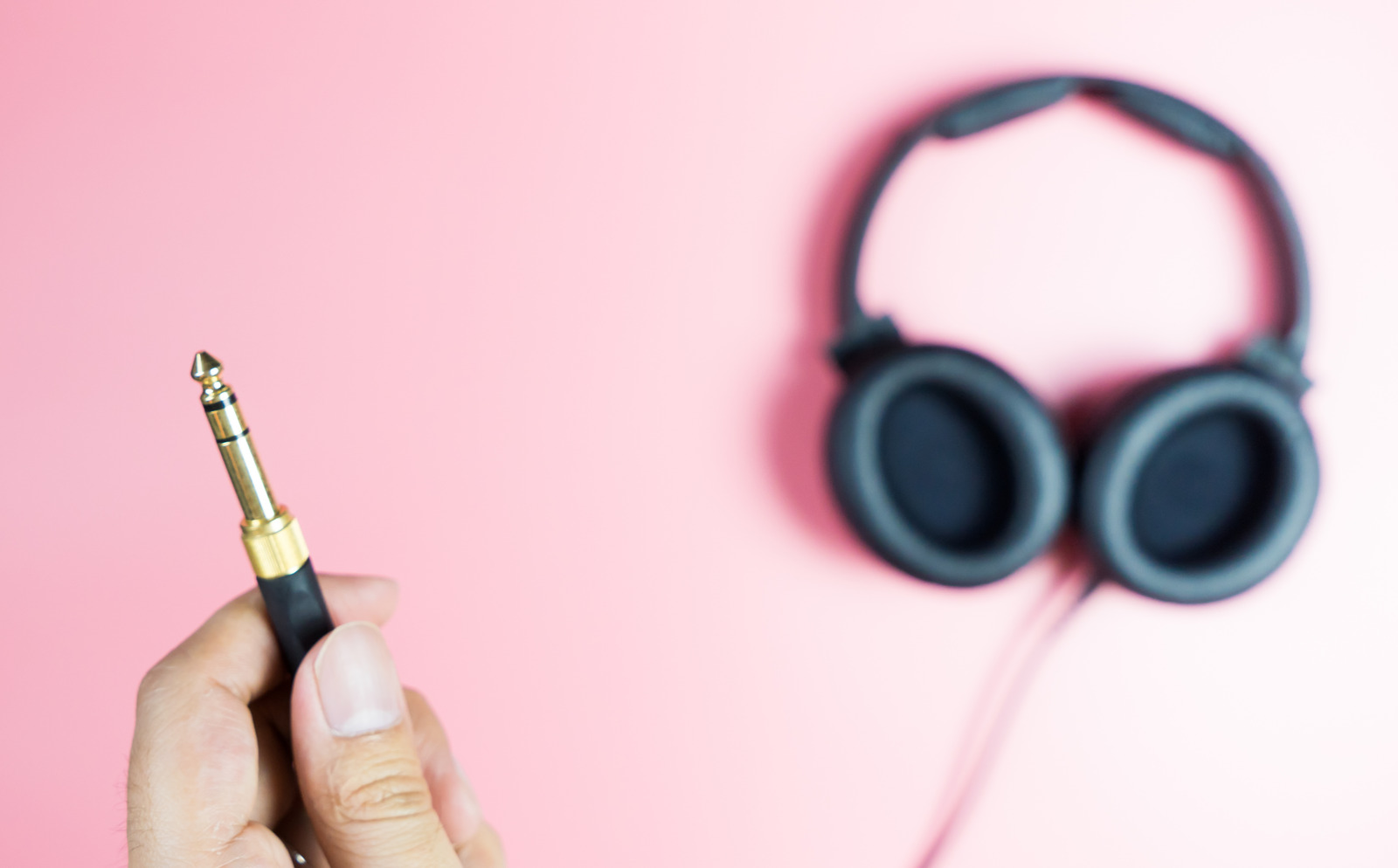Holding golden headphone jack on pink background
