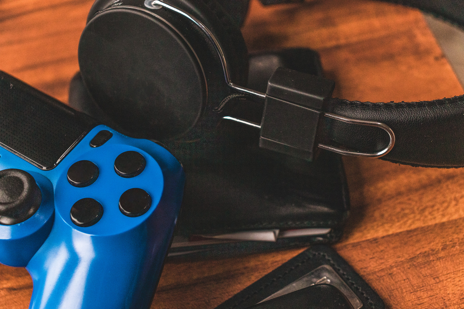 A close up shot of a blue games controller, headphones and wallet sitting on a wooden table.