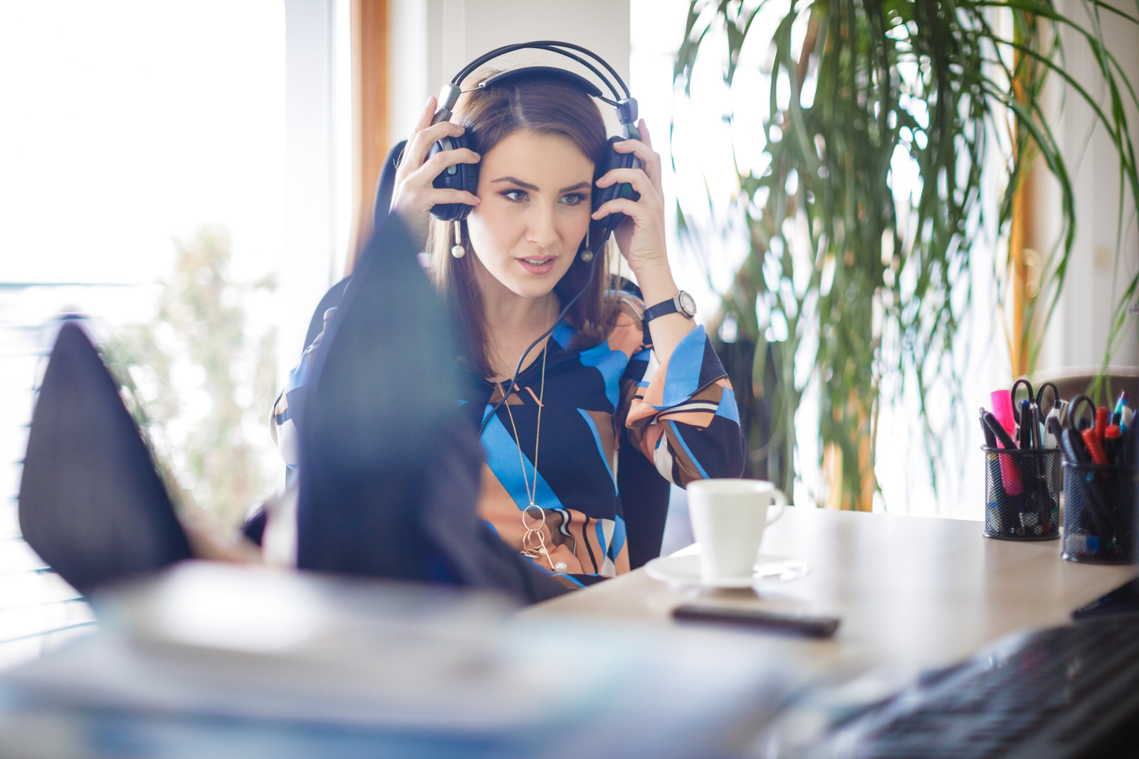 Smiling businesswoman on a break with feet up at her desk adjusting headphones