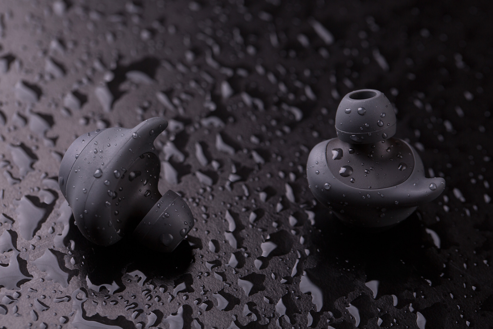 Intra-channel Bluetooth headphones on a dark background with water drops.