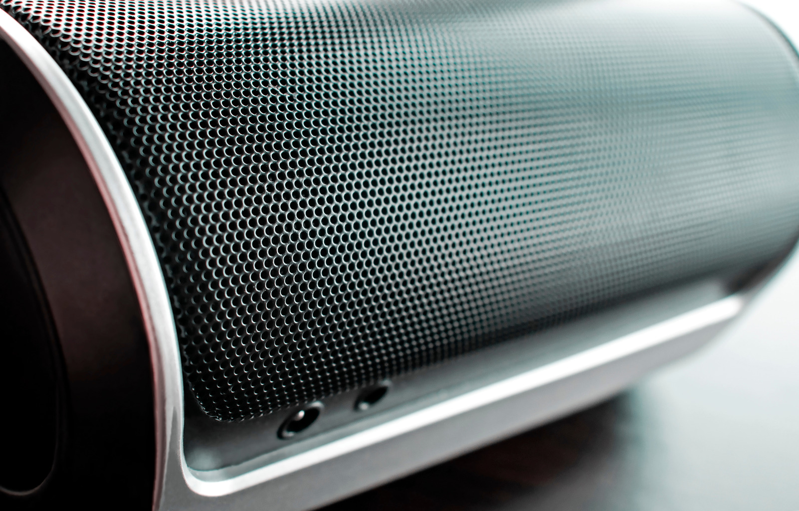 Close up angled photo of a black bluetooth rounded speaker showing the many holes in sharp focus in the foreground and gradually becoming soft in focus toward the background where the light becomes brighter