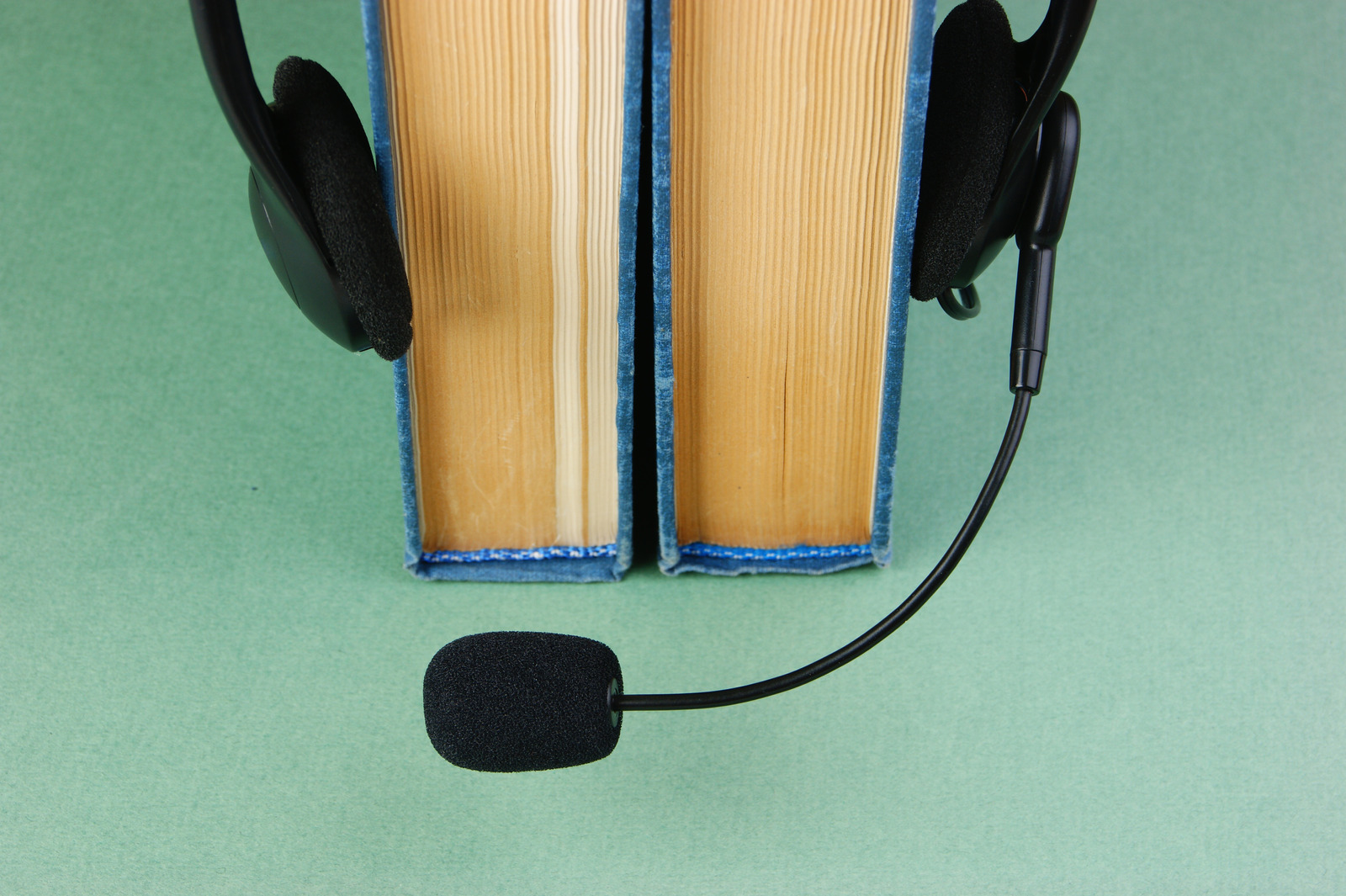 Headphones with a microphone and a stack of books on a green background
