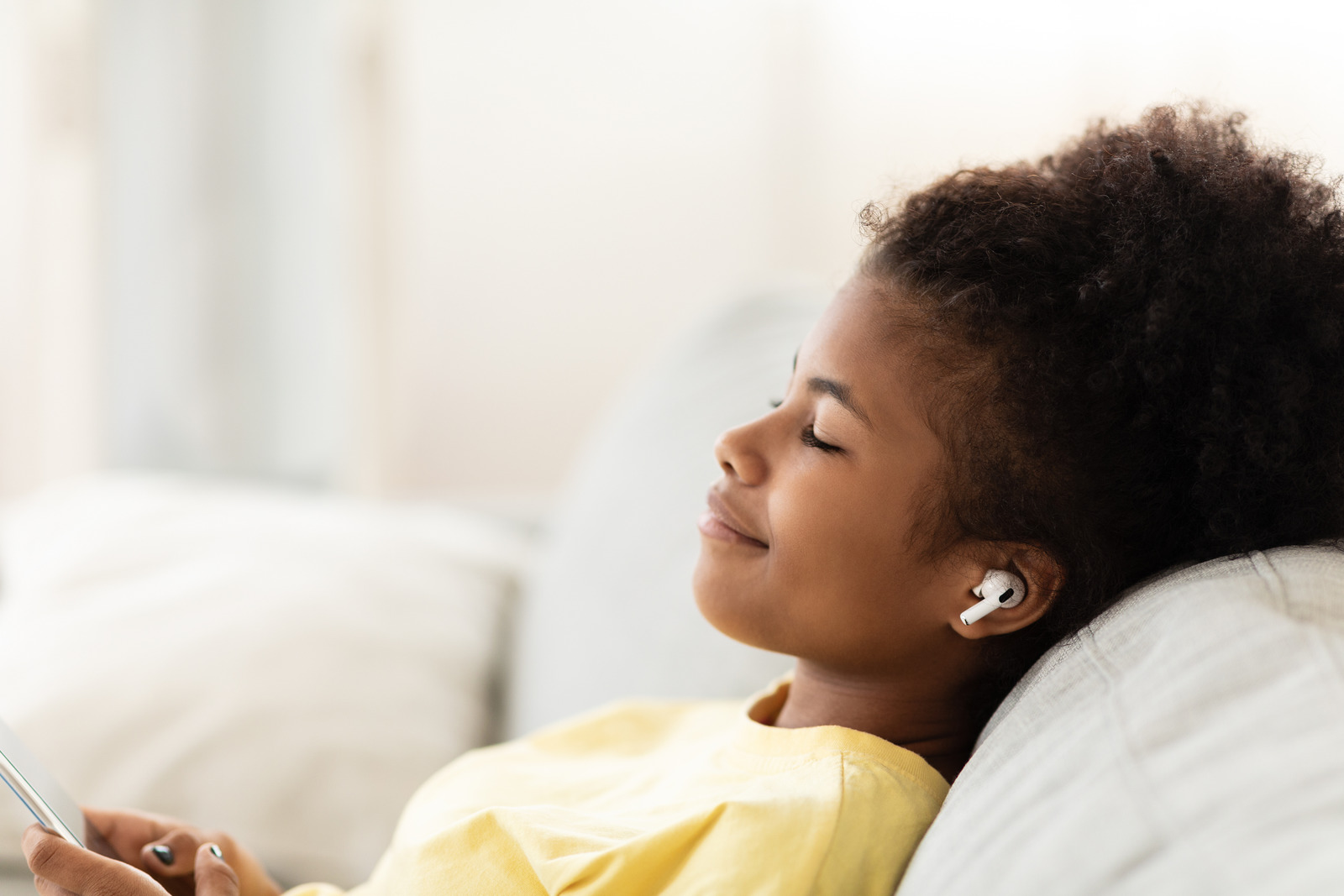 Black Teen Girl Listening To Music Wearing Earbuds Earphones Relaxing Sitting On Couch At Home. Free Space