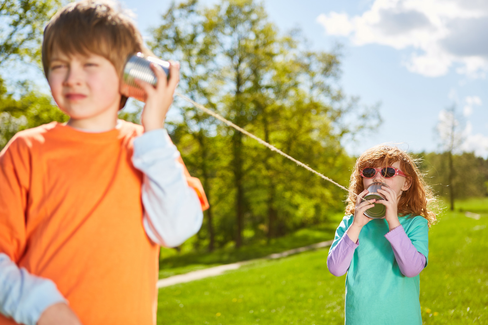 Two children communicate with a corded telephone in a park