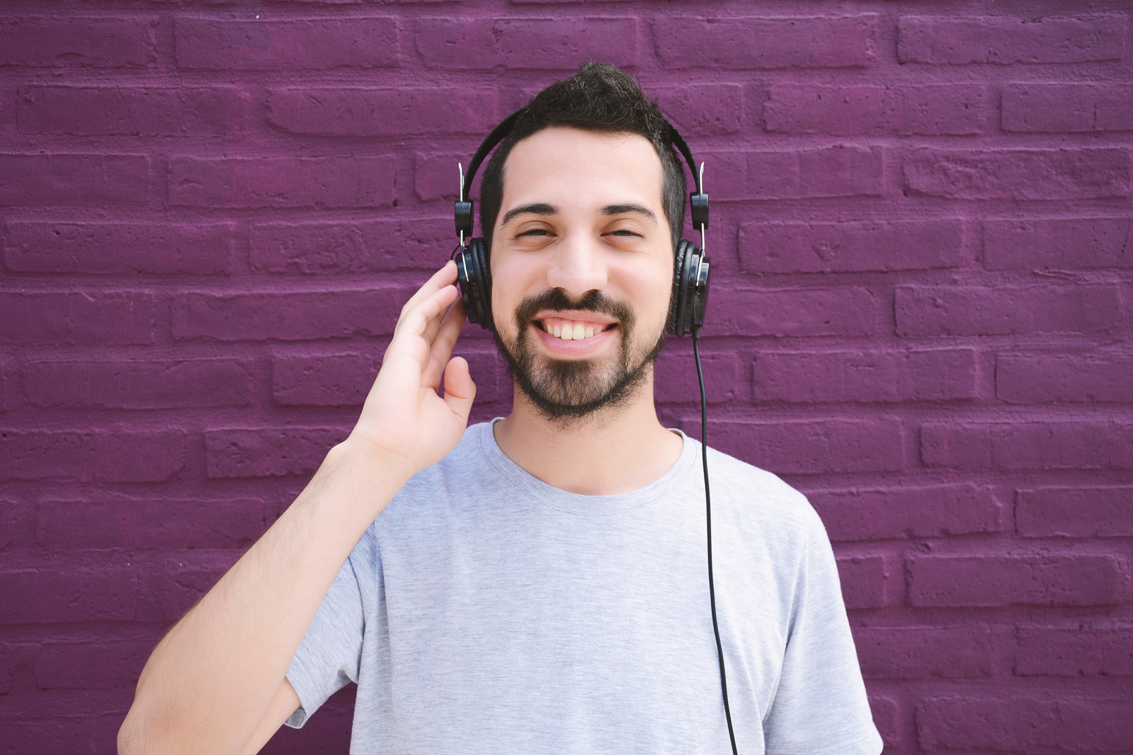 Portrait of young latin man listening to music with headphones. Outdoors.
