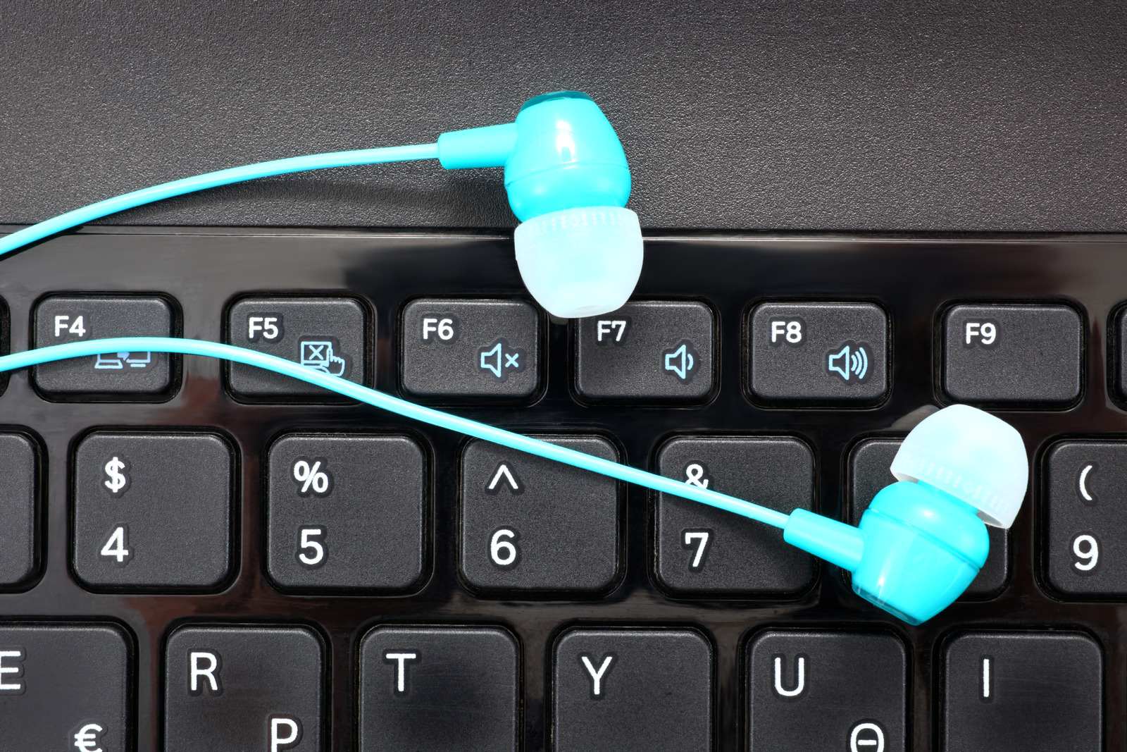 Blue headphones on a laptop keyboard with loudspeaker signs - digital music concept.