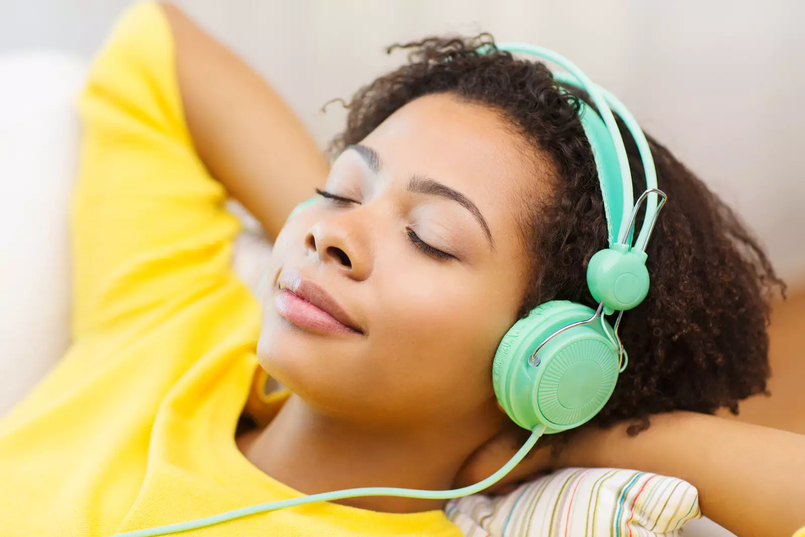 people, technology and leisure concept - happy african american young woman sitting on sofa with headphones listening to music at home