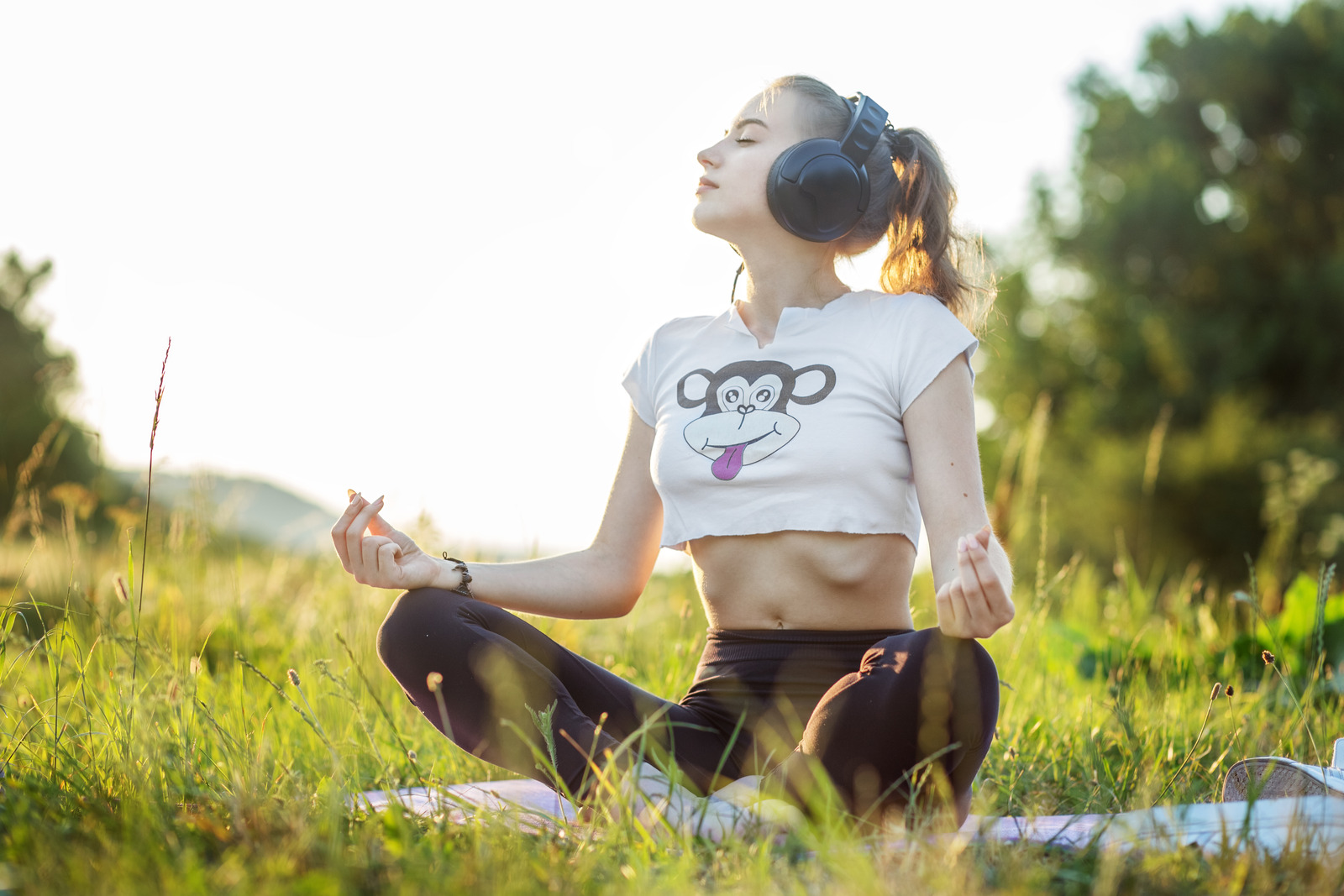 The girl listens to music on headphones. A woman is meditating. The combination of nature and man. Concept for lifestyle, music, relaxation.