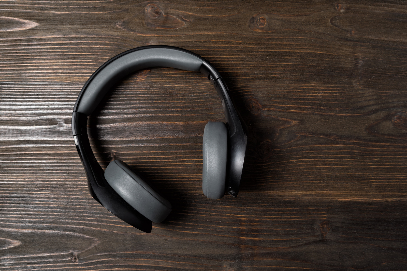 Black wireless earphones on a dark wooden background. Stereo headphones. Top view.