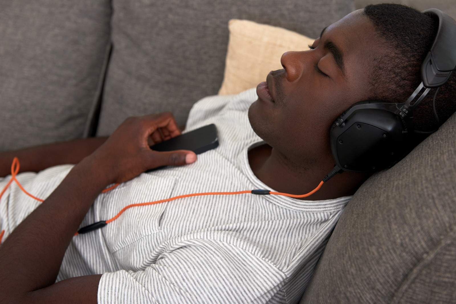 african black man listening to music relaxing on sofa couch in home living room