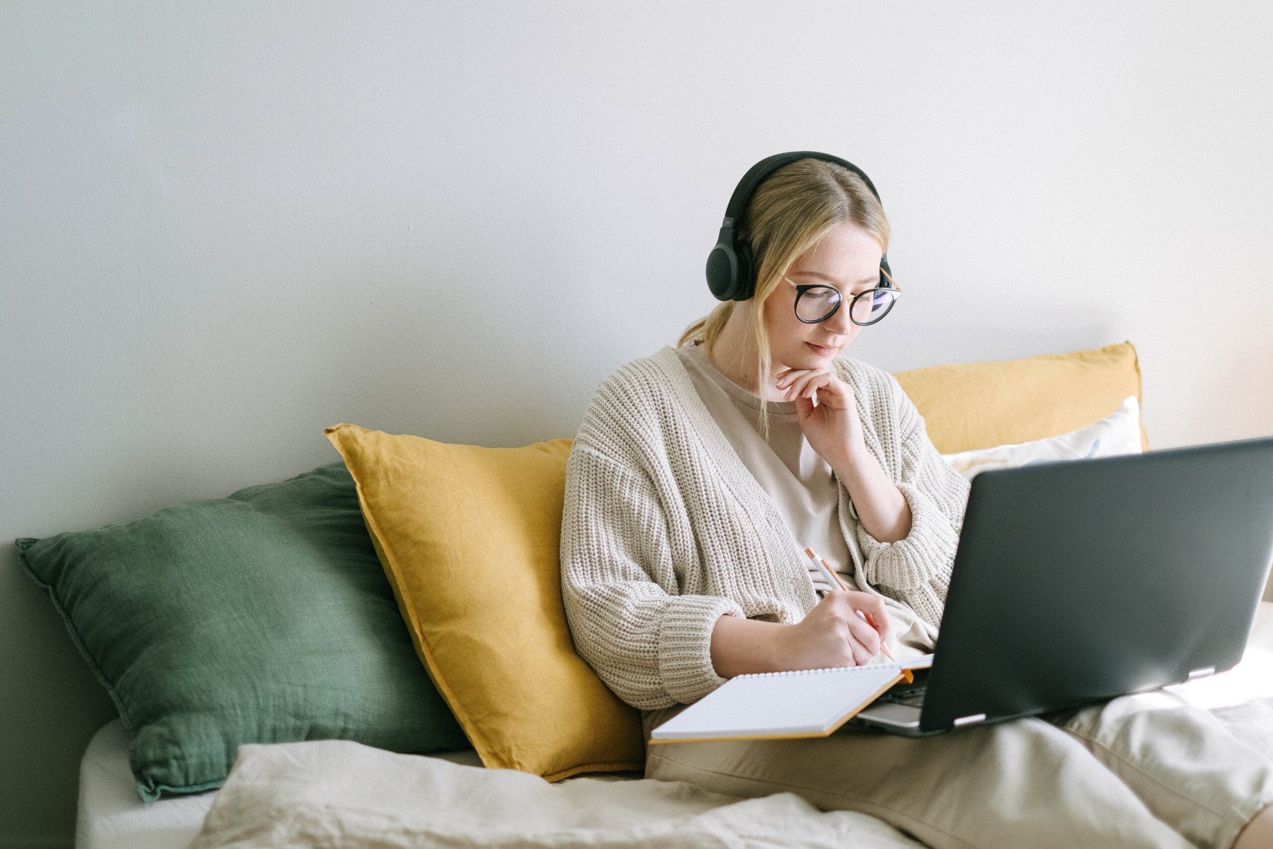 woman sitting on a bed using her laptop and headphones